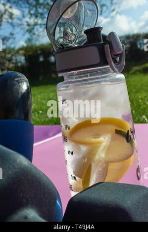 Una selezione di Kettlebells e manubri con una bottiglia di acqua fresca con calce e pezzi di limone in esso. Foto Stock