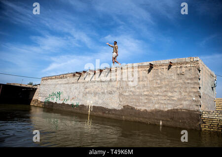 Khuzestan, Iran. Xiii Apr, 2019. Un uomo si erge sul tetto di una casa circondata da acqua di inondazione in un villaggio nella provincia di Khuzestan, Iran, il 13 aprile 2019. Le recenti inondazioni in più parti di Iran ha ucciso almeno 76 persone, premere il tasto TV ha riferito di domenica. Credito: Ahmad Halabisaz/Xinhua/Alamy Live News Foto Stock