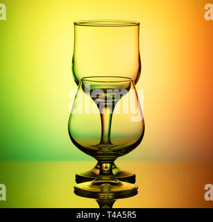 Bicchieri per il vino e il cognac con un contorno sottile stand arches dopo l'altro, su un luminoso giallo-sfondo verde Foto Stock