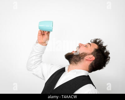 Bello, giovane con barba nera in posa con il turchese tazza di caffè o di tè cup davanti a uno sfondo bianco e produrre diverse espressioni del viso Foto Stock