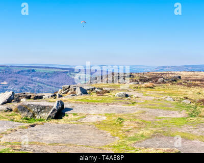 Parapendio vola oltre il bordo Curbar, nel Derbyshire Peak District, su un vago giornata di primavera. Foto Stock