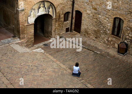 Una donna si siede nel grazioso cortile del Palazzo del Popolo prese dalla loggia, San Gimignano, Toscana, Italia. Modello rilasciato Foto Stock