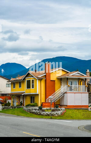 Giallo casa familiare con vista di montaggio su sfondo con cielo nuvoloso. Foto Stock