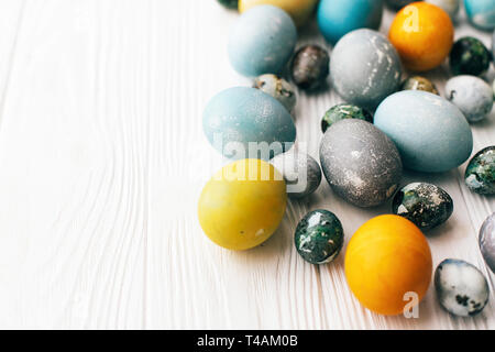 Elegante le uova di Pasqua di frontiera in bianco sullo sfondo di legno, copia dello spazio. Moderno uova pasquali dipinte con colorante naturale in giallo,blu,verde,colori grigi. Felice Foto Stock