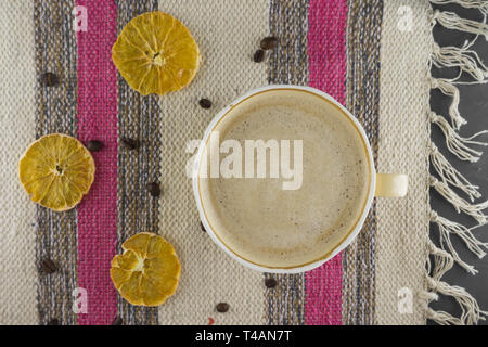 Una tazza di caffè in un accogliente stile su un tessuto a righe dello sfondo. Fette di arancia secca e i chicchi di caffè. Lay piatto. Foto Stock