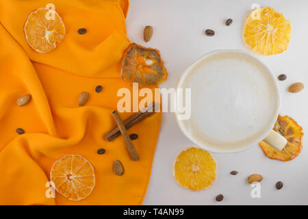 Una tazza di caffè in un accogliente stile su uno sfondo bianco e di un tessuto di colore arancione. Fette di arancia essiccata e kaki. Lay piatto. Foto Stock