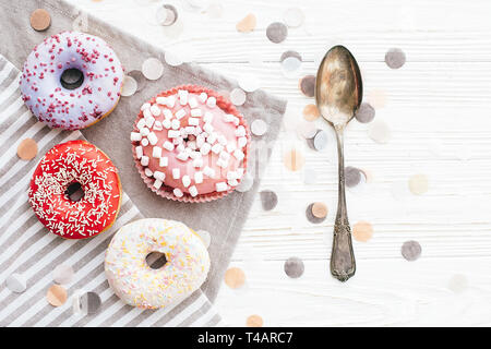 Deliziose ciambelle colorate con un pizzico e marshmallows su elegante tavolo bianco con i confetti e cucchiaio vintage, piatto laici. Il concetto di partito. Nessuna dieta. Ca Foto Stock