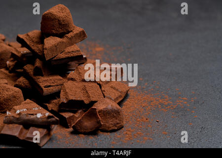 Dark o latte organico pezzi di cioccolato, polvere di cacao e tartufo caramelle sul calcestruzzo scuro sfondo Foto Stock