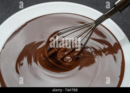 Macro di latte fuso di cioccolato fondente o turbolenza nella piastra e frusta su sfondo di calcestruzzo Foto Stock