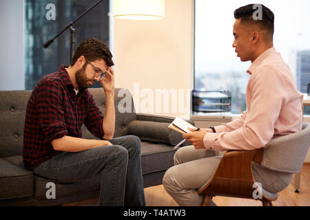 Uomo infelice seduta sul lettino incontro con il Consigliere maschio in Office Foto Stock