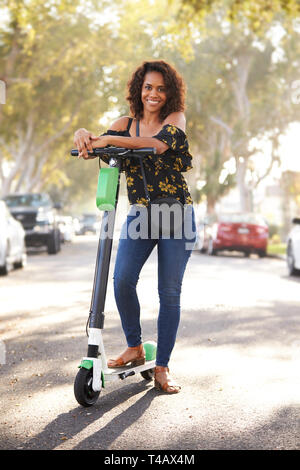 La millenaria nero donna in piedi in strada appoggiato su di un scooter elettrico,a lunghezza piena, close up Foto Stock