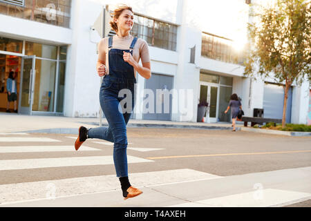 Moda giovane donna ispanica in salopette da corsa attraverso la strada a piena lunghezza e chiudere fino Foto Stock