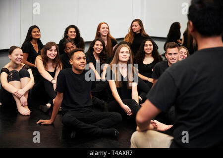 Insegnante al Performing Arts School a parlare con gli studenti seduti sul pavimento in prove di Studio Foto Stock