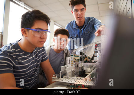 Insegnante con due maschi studenti del college Building Machine nella scienza robotica o classe di ingegneria Foto Stock