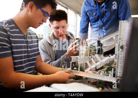 Insegnante con due maschi studenti del college Building Machine nella scienza robotica o classe di ingegneria Foto Stock