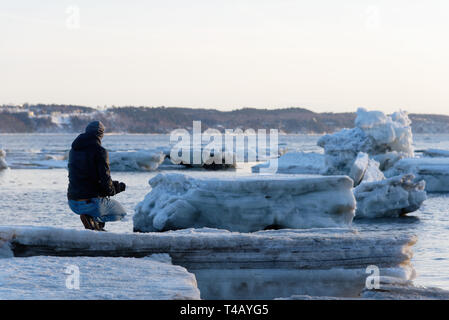 Un uomo inginocchiato sulla banchisa sulla riva del San Lorenzo a Cap Rouge, Quebec, Canada Foto Stock