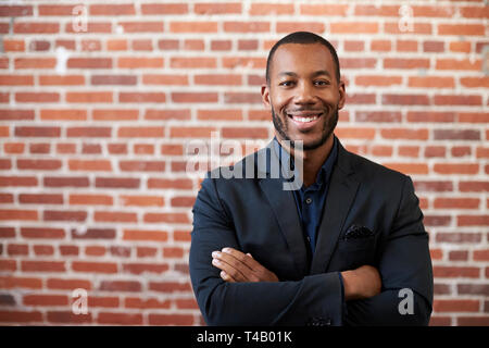 Ritratto di imprenditore in piedi contro un muro di mattoni in ufficio moderno Foto Stock