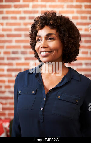 Sorridente imprenditrice matura in piedi contro un muro di mattoni in ufficio moderno Foto Stock