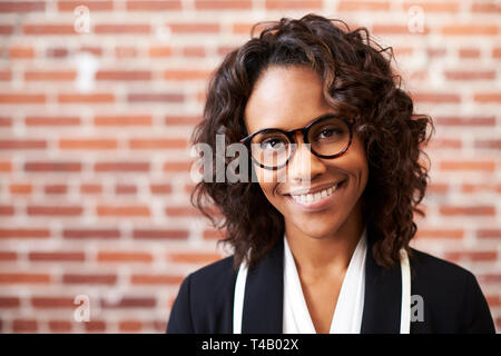 Ritratto di sorridere imprenditrice con gli occhiali in piedi contro un muro di mattoni in ufficio moderno Foto Stock