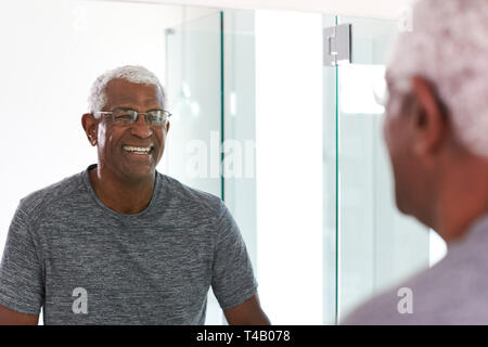 Sorridente uomo Senior guardando la riflessione nello specchio del bagno indossando pigiami Foto Stock