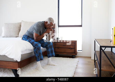 Premuto Senior cerca uomo infelice seduta sul lato del letto di casa con testa in mani Foto Stock