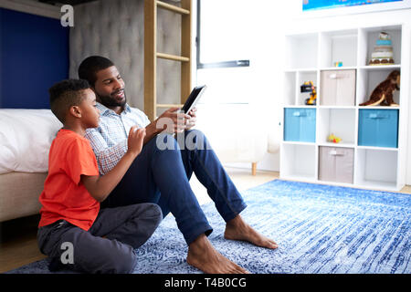 Padre con Figlio seduto in camera da letto un gioco sulla tavoletta digitale insieme Foto Stock