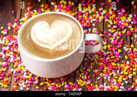 Tazza di forma di cuore del caffè su di un tavolo di legno con colorate caramelle dolci sani e freschi tè Foto Stock