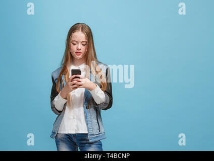 Tempo per nuove conoscenze. Una ragazza con uno smartphone in jeans tuta in piedi su sfondo blu. La tecnologia di riconoscimento facciale su griglia poligonale. Concetto di cyber security, business, lavoro, educazione. Foto Stock