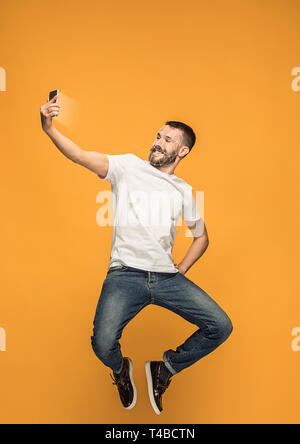 Cheking nuove opportunità. Un uomo con uno smartphone in jeans e maglietta bianca in esecuzione su sfondo giallo. La tecnologia di riconoscimento facciale su griglia poligonale. Concetto di cyber security, business, lavoro. Foto Stock