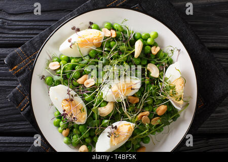 Deliziosa insalata sana di piselli verdi, micro verdi, i dadi e le uova cotte su una piastra sul tavolo. parte superiore orizzontale vista da sopra Foto Stock