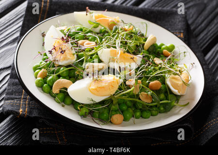 Molla verde insalata di piselli, micro verdi, i dadi e le uova di close-up su una piastra sul tavolo orizzontale. Foto Stock