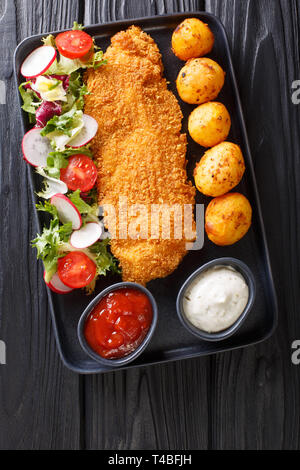 Corso principale di filetti di merluzzo in panatura con una decorazione di patate di primizia e fresca insalata di verdure close-up su una piastra sul tavolo. Verticale in alto visualizza fro Foto Stock