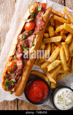 Deliziosi hot dog con pancetta e verdure servita con patatine fritte e salse close-up sul tavolo. Verticale in alto vista da sopra Foto Stock