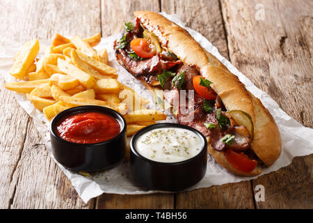 Piccante tradizionale di hot dog con pancetta fritta, verdure, patatine fritte e salse close-up sul tavolo orizzontale. Foto Stock