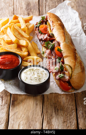 Stile rustico di hot dog con pancetta e verdure servita con patatine fritte e salse close-up sul piano verticale. Foto Stock