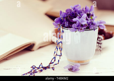 Ancora in vita con violetta in tazza bianca, vecchi libri. Molla romantico sfondo floreale. Foto Stock