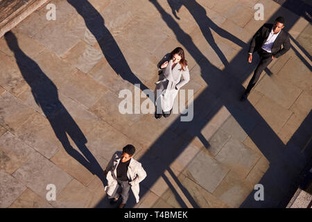 Vista aerea di tre persone di affari a piedi nella stessa direzione su una soleggiata strada urbana, orizzontale Foto Stock