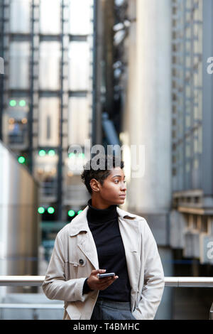 Giovane imprenditrice nero in piedi in città con lo smartphone in mano, close up, verticale Foto Stock