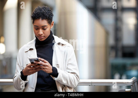Giovane donna adulta in piedi in una zona business della città con il suo smartphone, la messa a fuoco su oggetti in primo piano Foto Stock