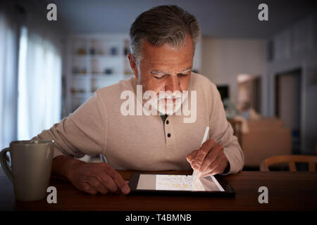 Senior uomo ispanico si siede a tavola utilizzando lo stilo e tablet pc a casa di sera, close up Foto Stock