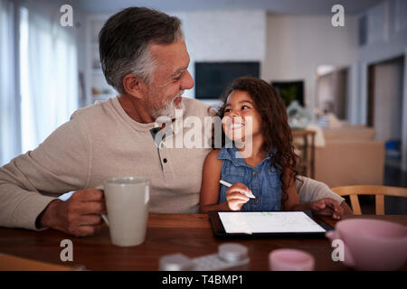 Senior uomo ispanico con la sua nipote utilizzando computer tablet, guardando ogni altro, vista frontale Foto Stock