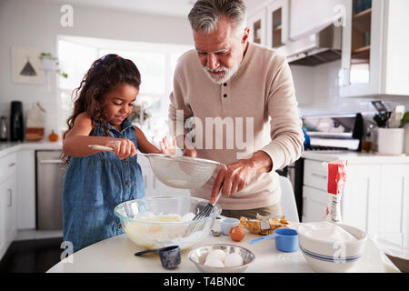 Ragazza giovane la preparazione di miscela per torte con suo nonno al tavolo della cucina, close up Foto Stock