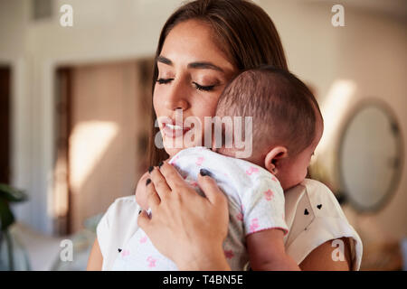 Millenaria madre ispanica con gli occhi chiusi, tenendo il suo figlio neonato al petto, close up Foto Stock