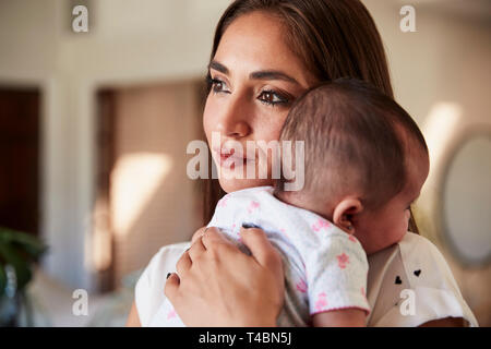 Millenaria madre ispanica tenendo il figlio neonato vicino al petto, testa e spalle, close up Foto Stock