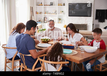 Tre generazioni della famiglia ispanica seduta al tavolo tenendo le mani e dicendo la grazia prima di cena Foto Stock