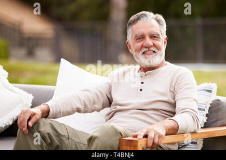 Felice ispanica senior uomo seduto su un sedile in giardino a sorridere alla telecamera, close up Foto Stock