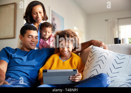 Giovane famiglia di trascorrere del tempo insieme utilizzando un computer tablet nel loro soggiorno, vista frontale Foto Stock