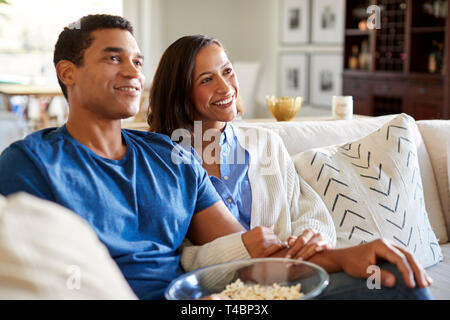 Felice razza mista millenaria giovane seduto sul divano nel loro salotto guardando la TV e mangiare popcorn, close up Foto Stock
