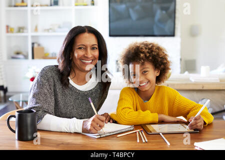 Persone di mezza età razza mista donna seduta al tavolo nella sua sala da pranzo il disegno con la sua pre-teen nipote, sorridente alla telecamera, vista frontale, close up Foto Stock