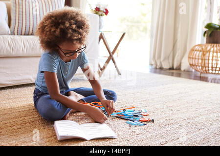 Pre-teen ragazza seduta sul pavimento del salotto istruzioni di lettura e la costruzione di un modello, close up Foto Stock